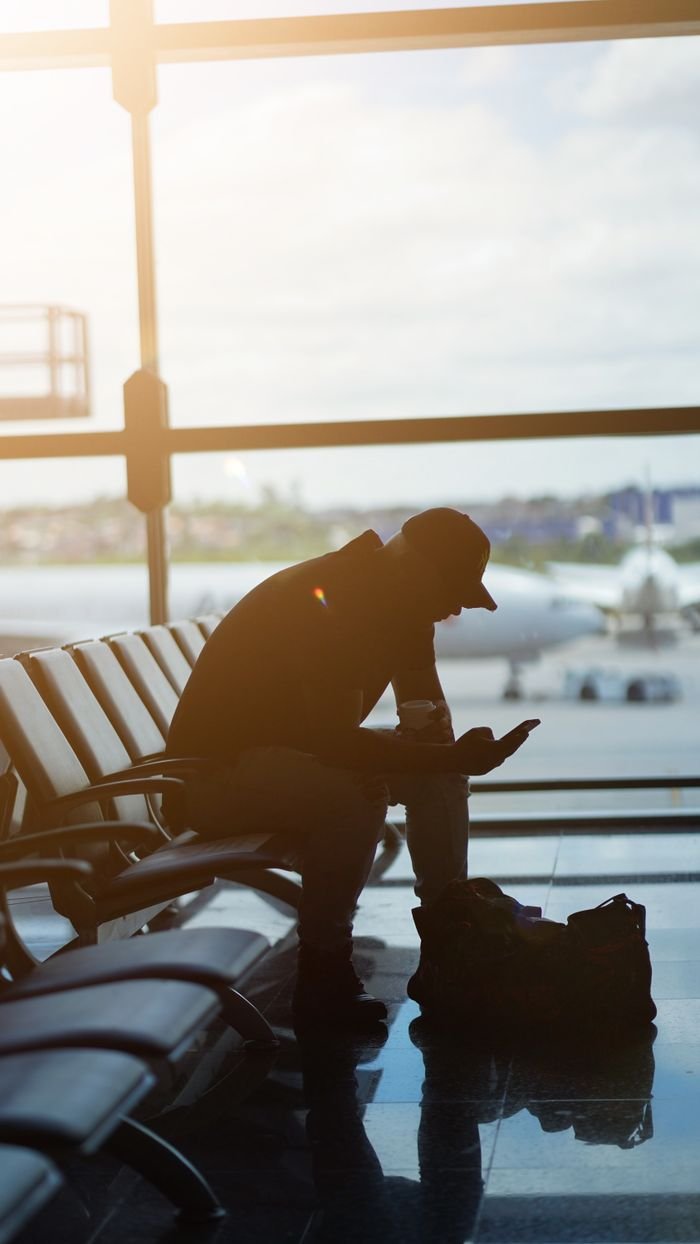 The Art of Drawing Readers In: Your attractive post title goes here Silhouette of a man using a smartphone in an airport waiting area with airplanes visible outside.
