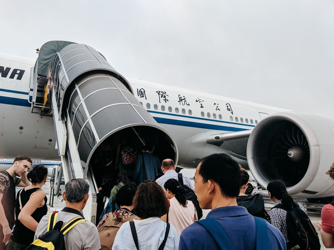 Home A group of people boarding an airplane via a jet bridge at Beijing Airport, China.