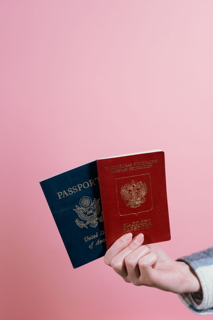 Home Close-up of two passports held by a hand against a pink background.